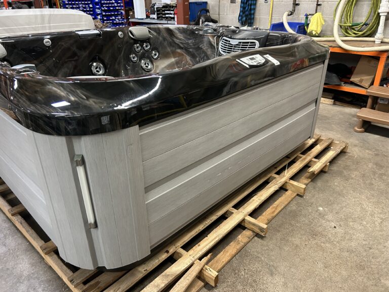 Jacuzzi J-355 hot tub front view with gray cabinet and dark acrylic shell on warehouse floor